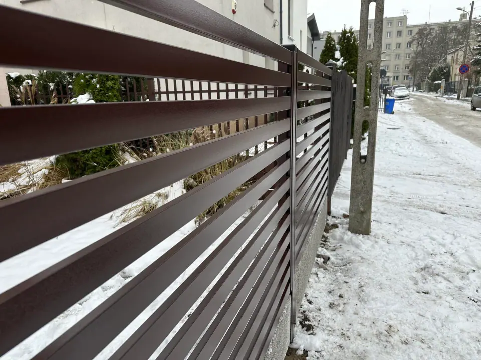 Brązowe poziome profile ogrodzenia palisadowego z widocznymi prześwitami